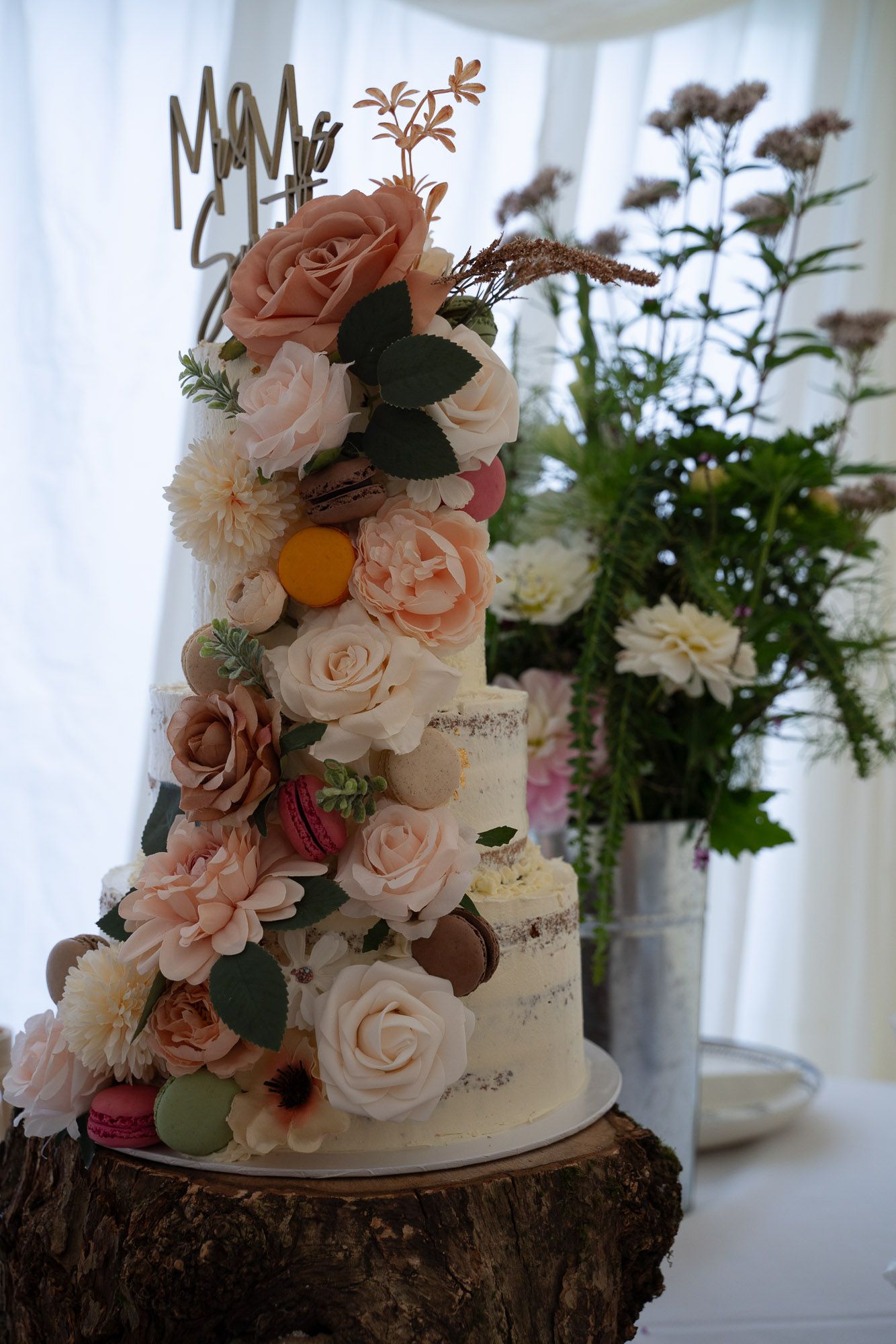 Beautiful tiered white wedding cake adorned with blush roses and greenery on rustic wood stand.
