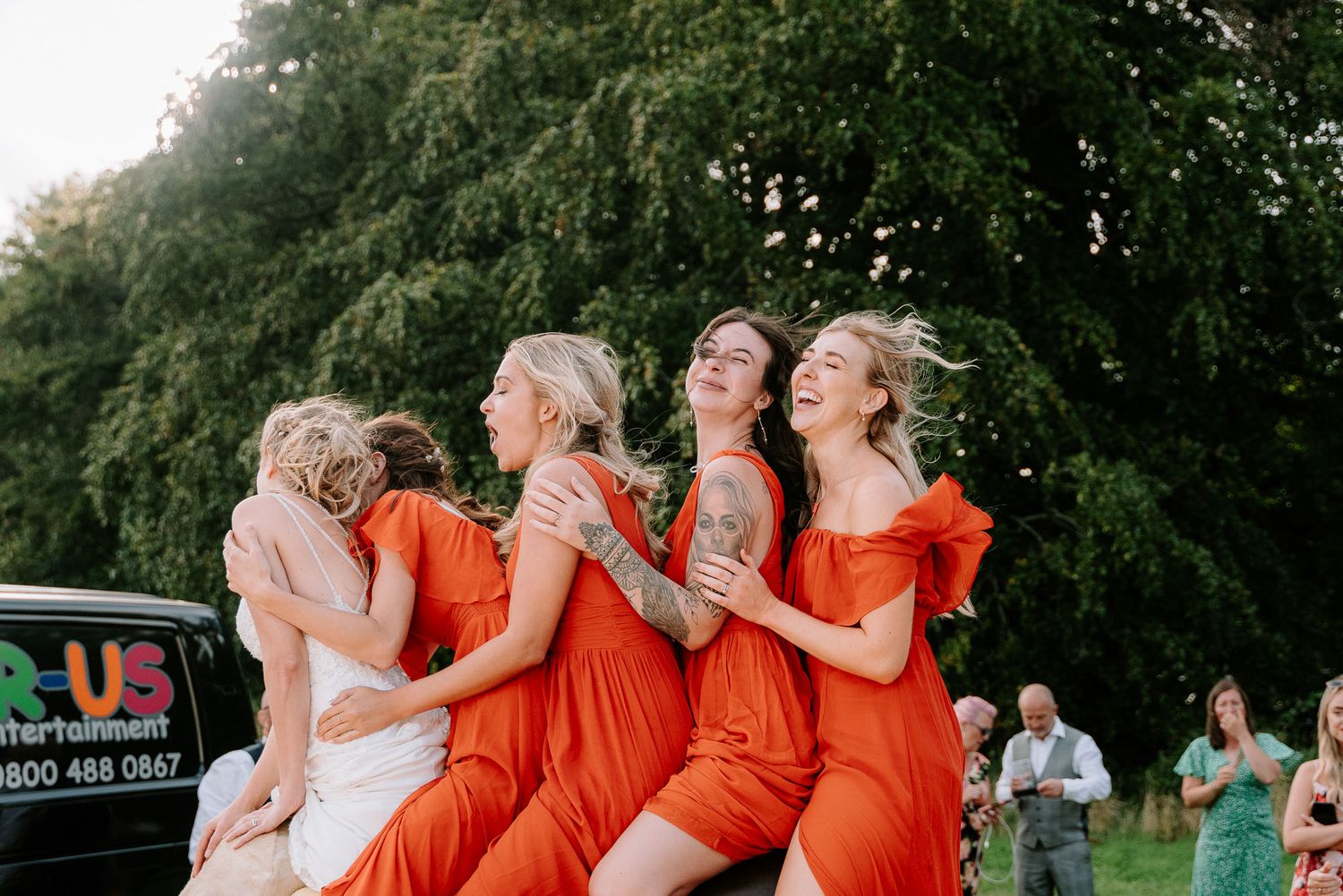 Wedding party in orange dresses poses together outdoors in a natural setting.