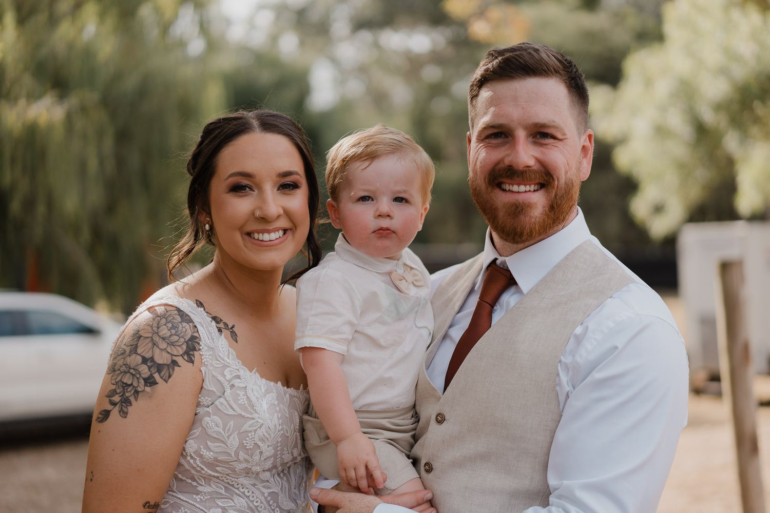 Wedding couple poses with young child in outdoor setting.