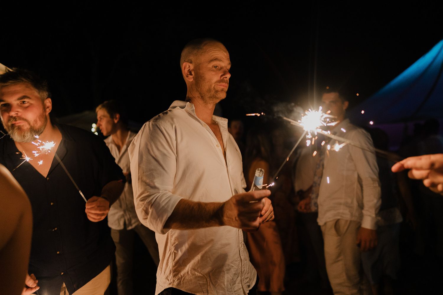 People hold sparklers creating a magical nighttime atmosphere at an outdoor celebration.