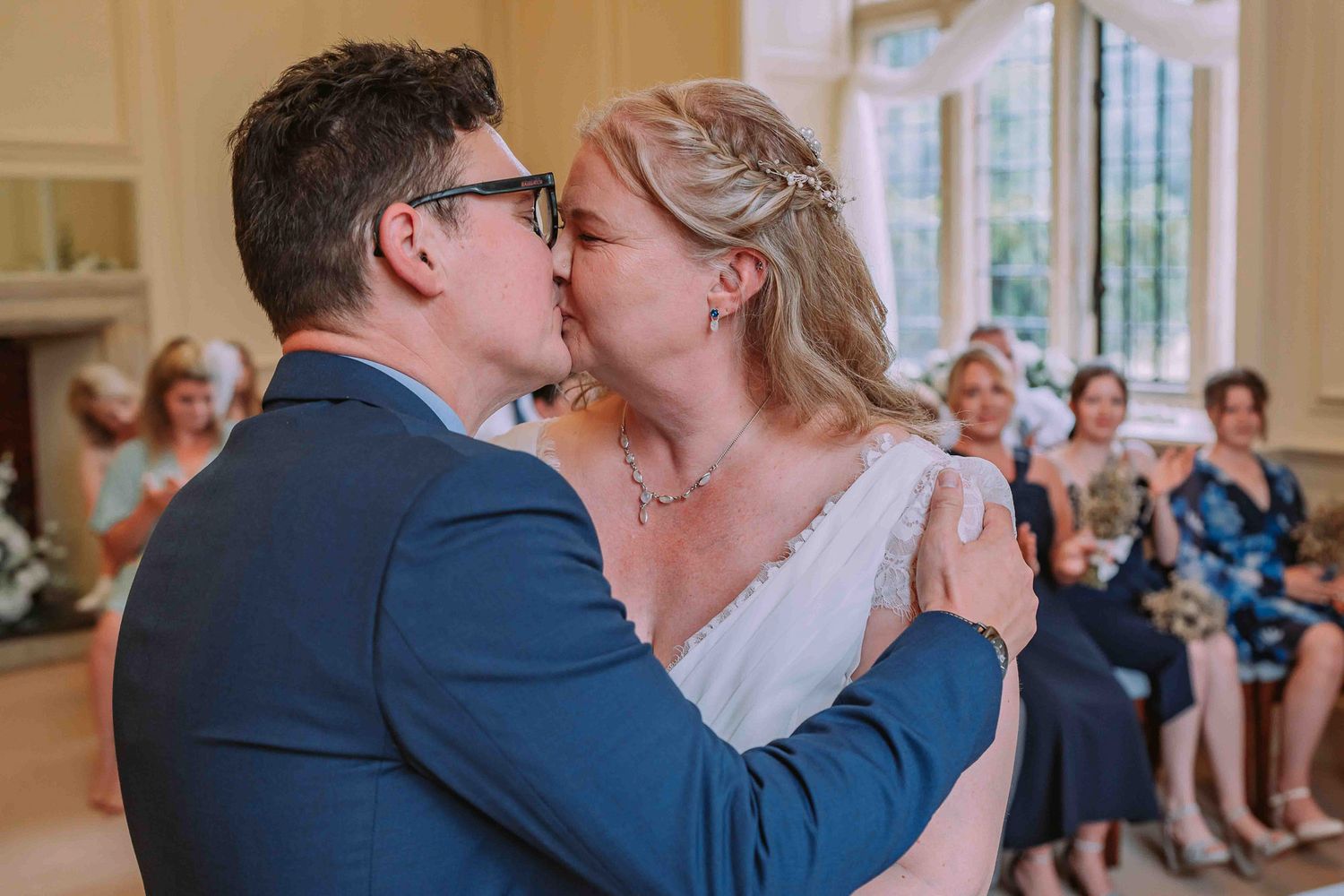 Romantic moment captured inside an elegant venue with guests watching in background.