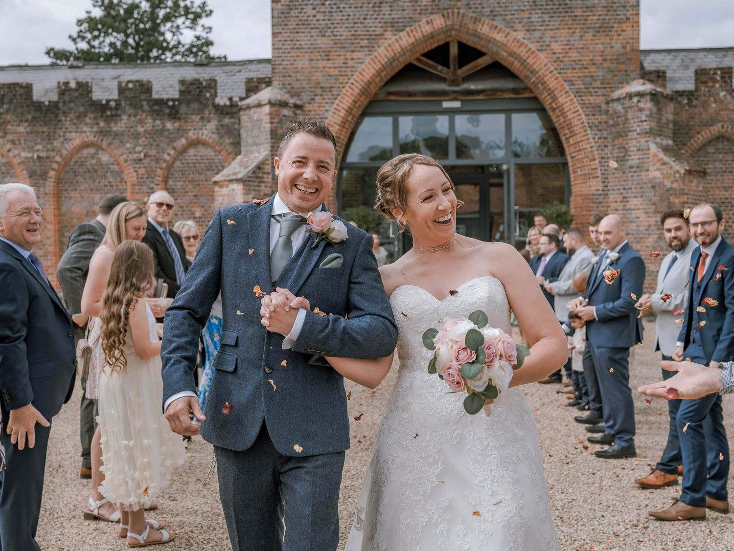 Wedding party gathers outside historic brick church with arched doorway.