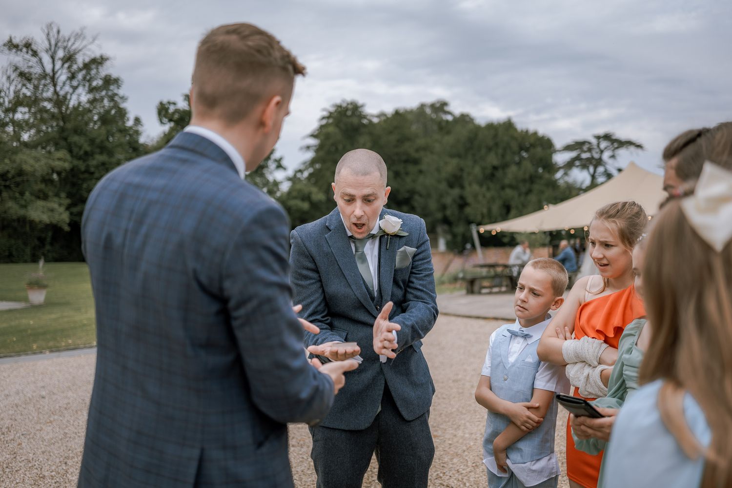 Wedding guests mingle outside on rustic grounds during daytime celebration.
