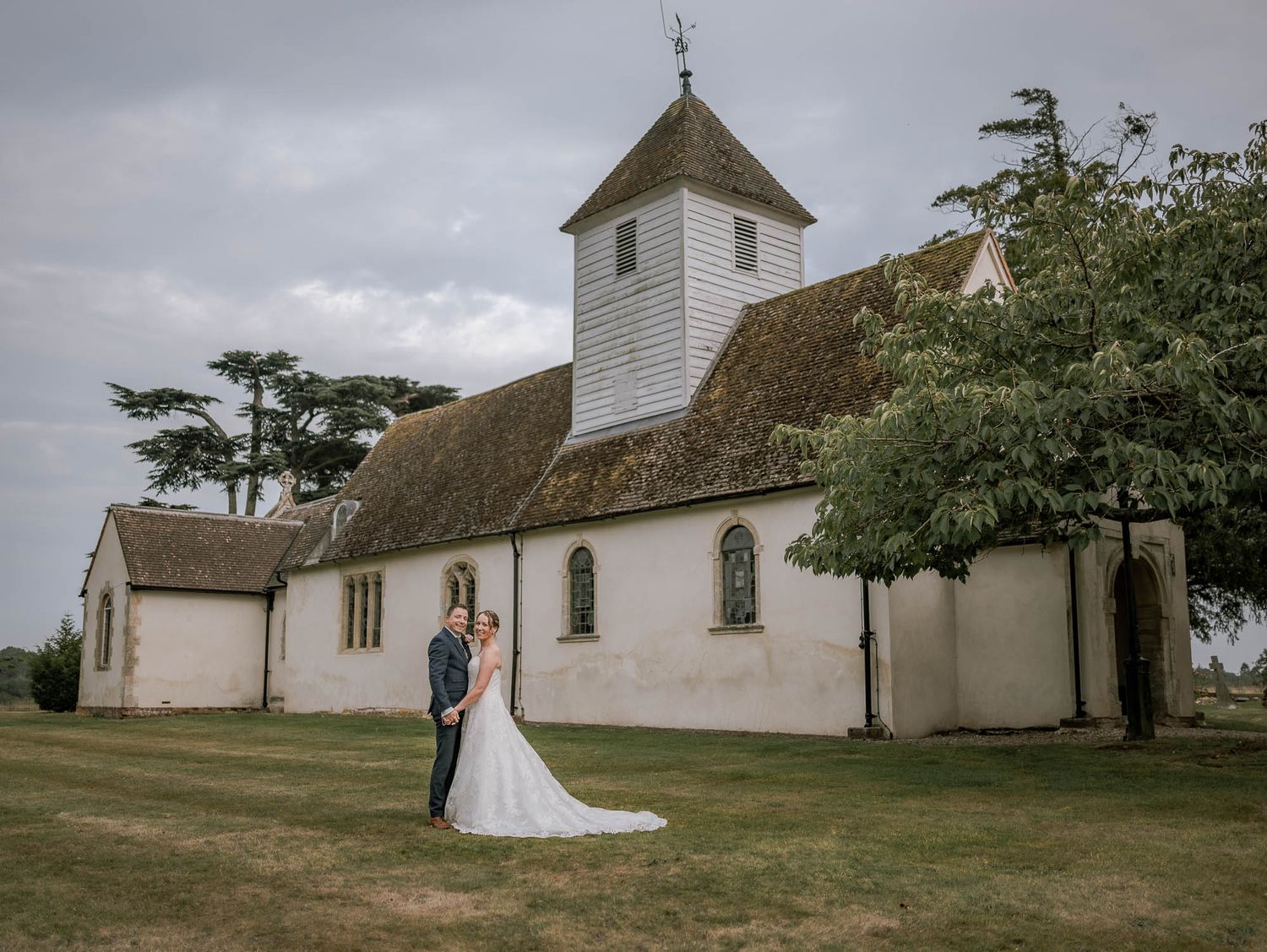 White church building stands against cloudy sky on grassy landscape.