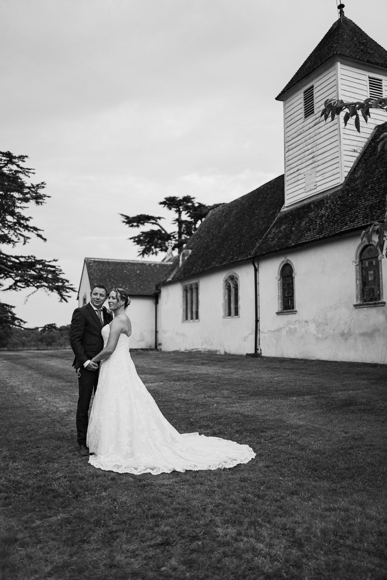 Black and white photo of couple posing outside traditional white church building.