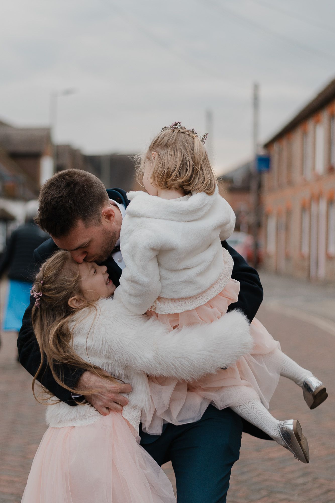 Playful couple in formal wear spinning and embracing on a brick street.