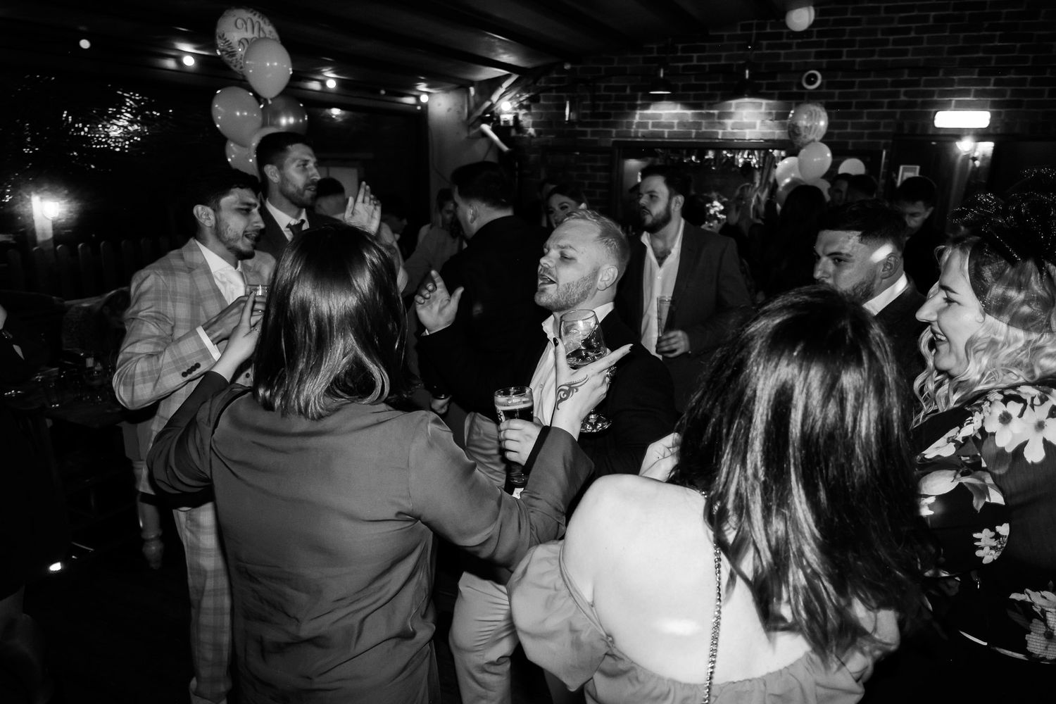 Party guests dancing and mingling in a dark indoor venue with atmospheric lighting.