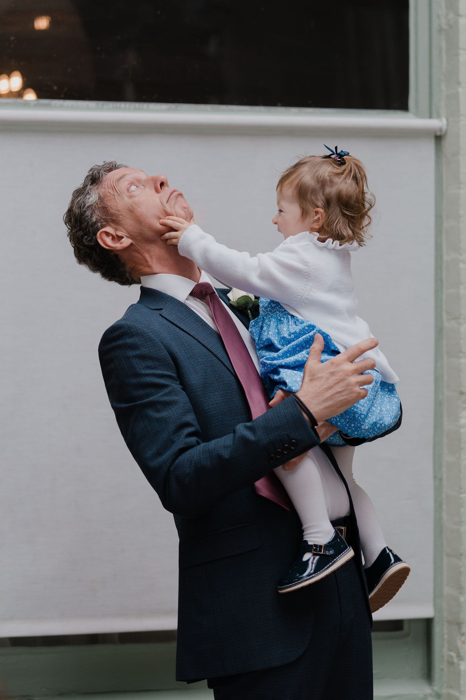 A playful moment at a wedding reception shows a guest lifting a small child in formal attire.