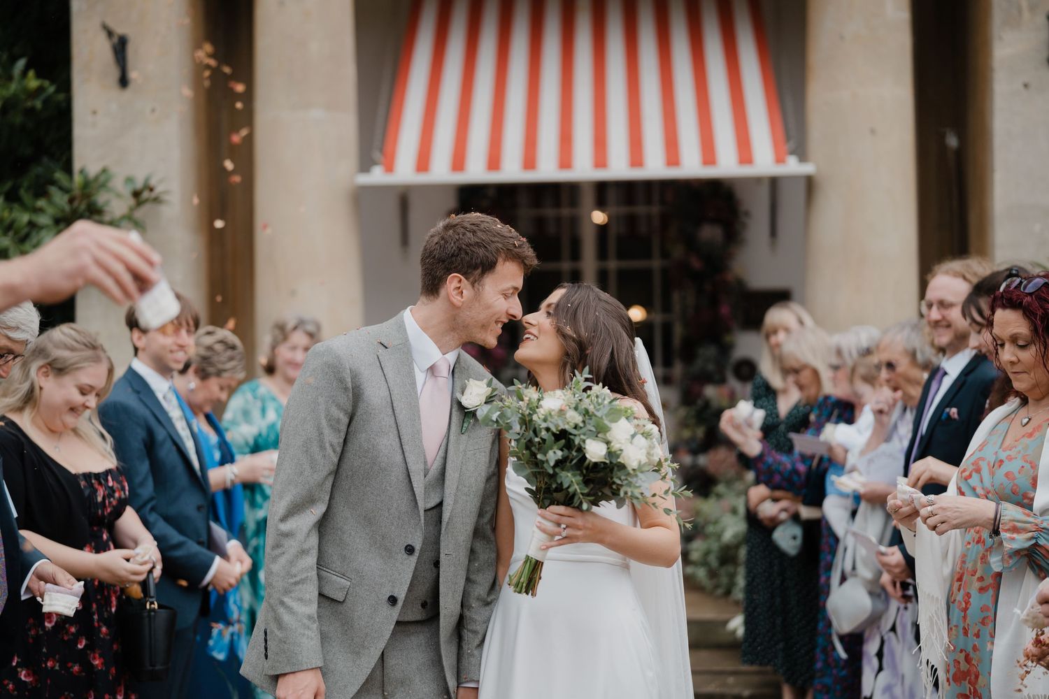 Wedding celebration under a striped awning with floral decorations and string lights.