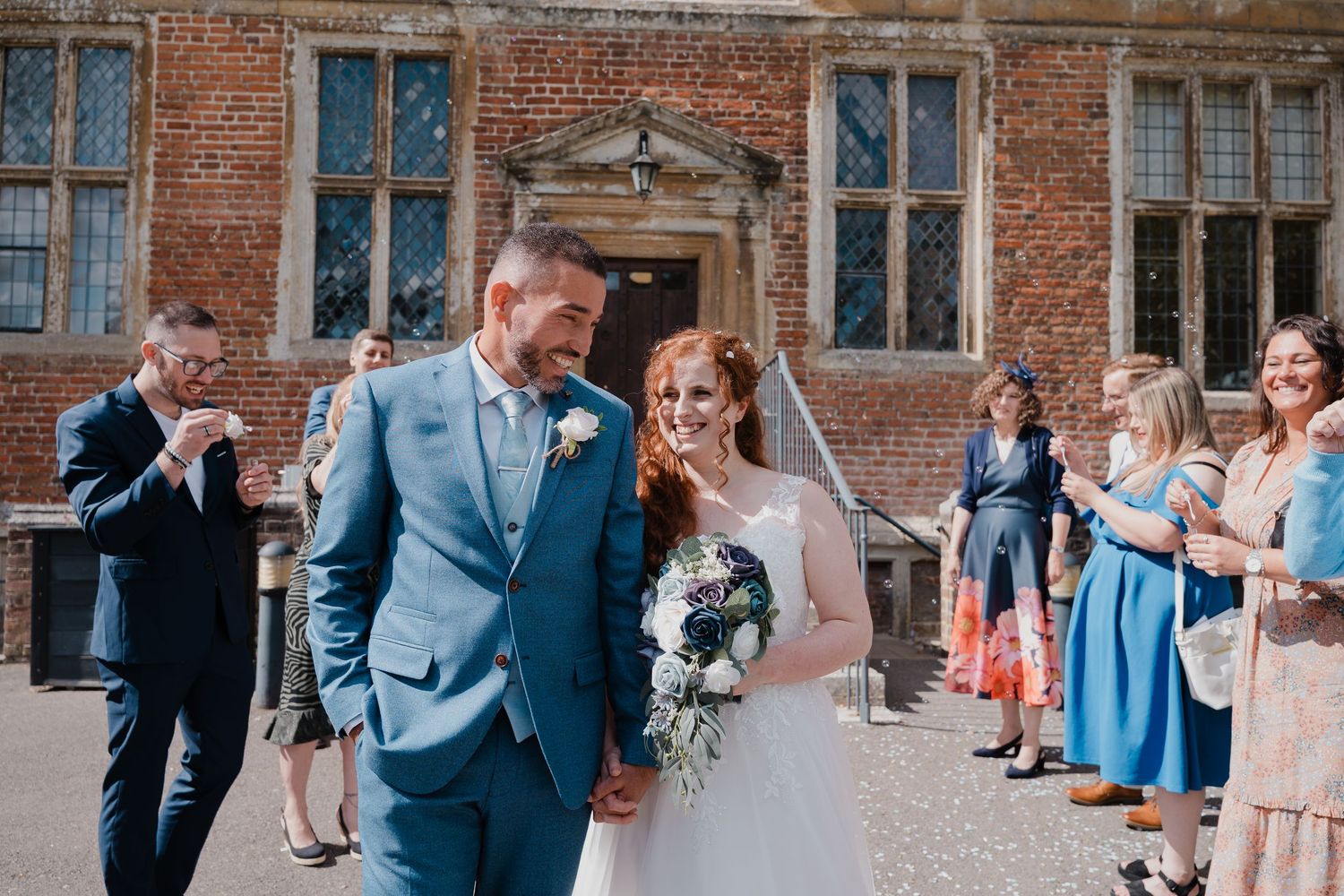 Wedding celebration outside a grand brick building with guests throwing confetti.