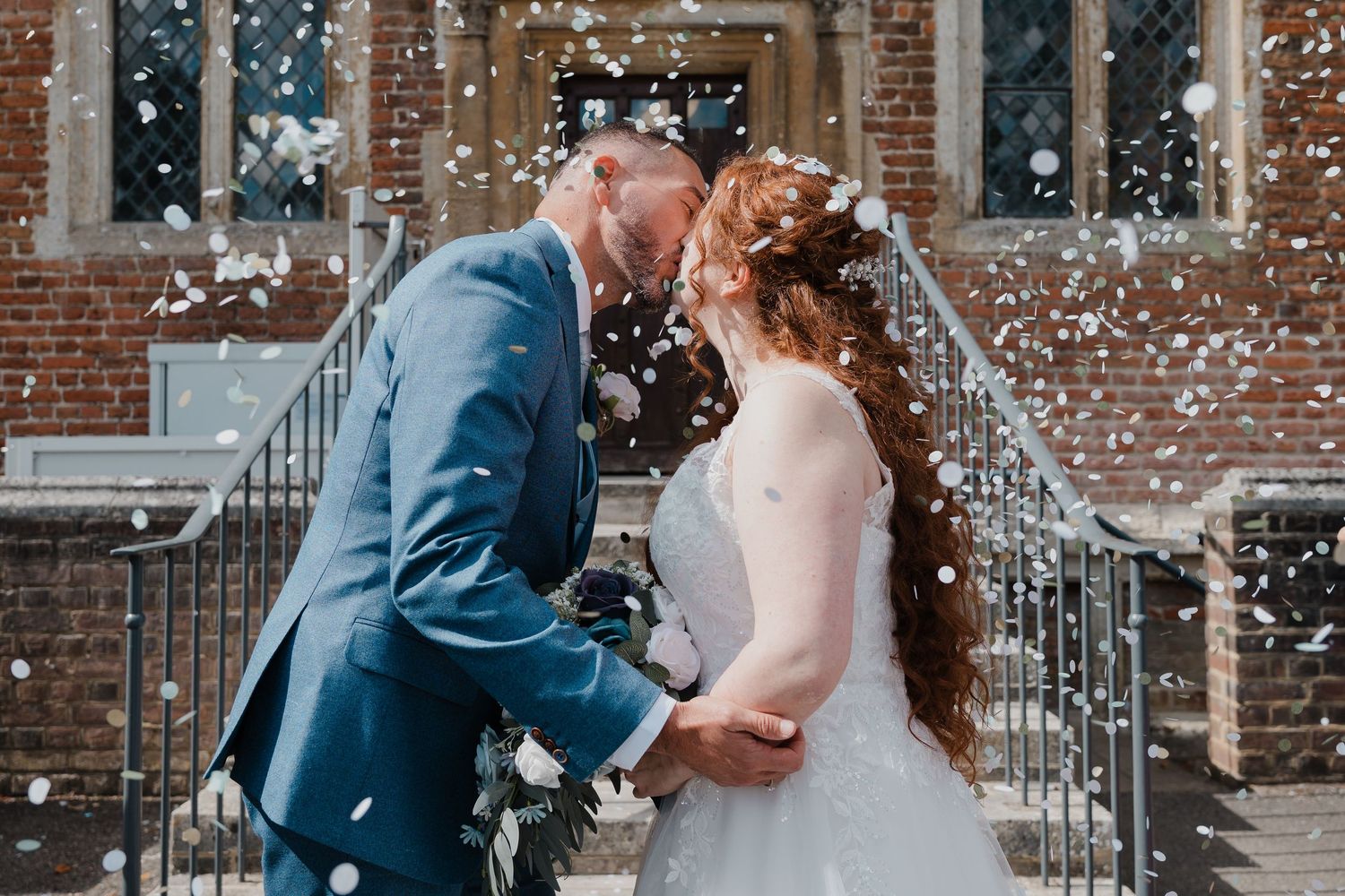 Newlyweds celebrate with confetti outside a historic brick building.