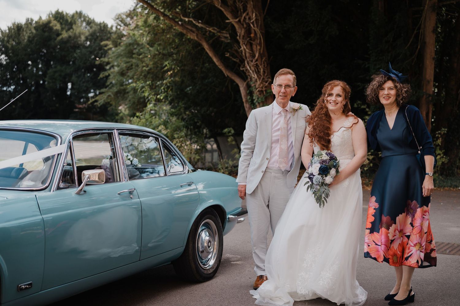 Wedding party poses beside a classic light blue vintage car.