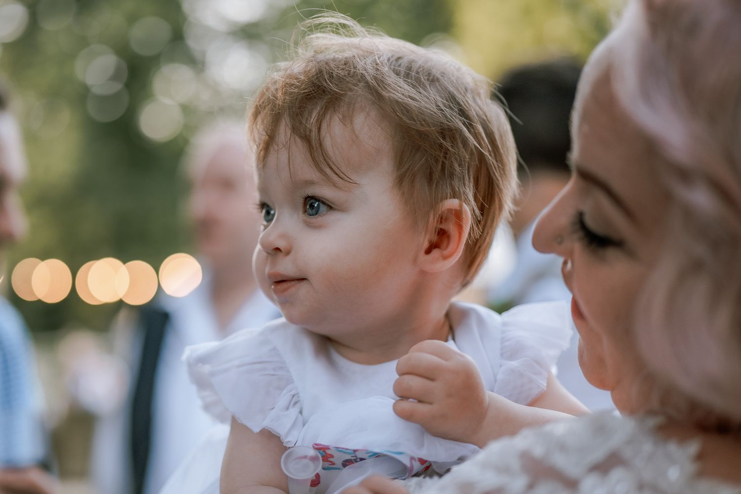 Wedding guests gathered outdoors with natural bokeh lighting in the background.