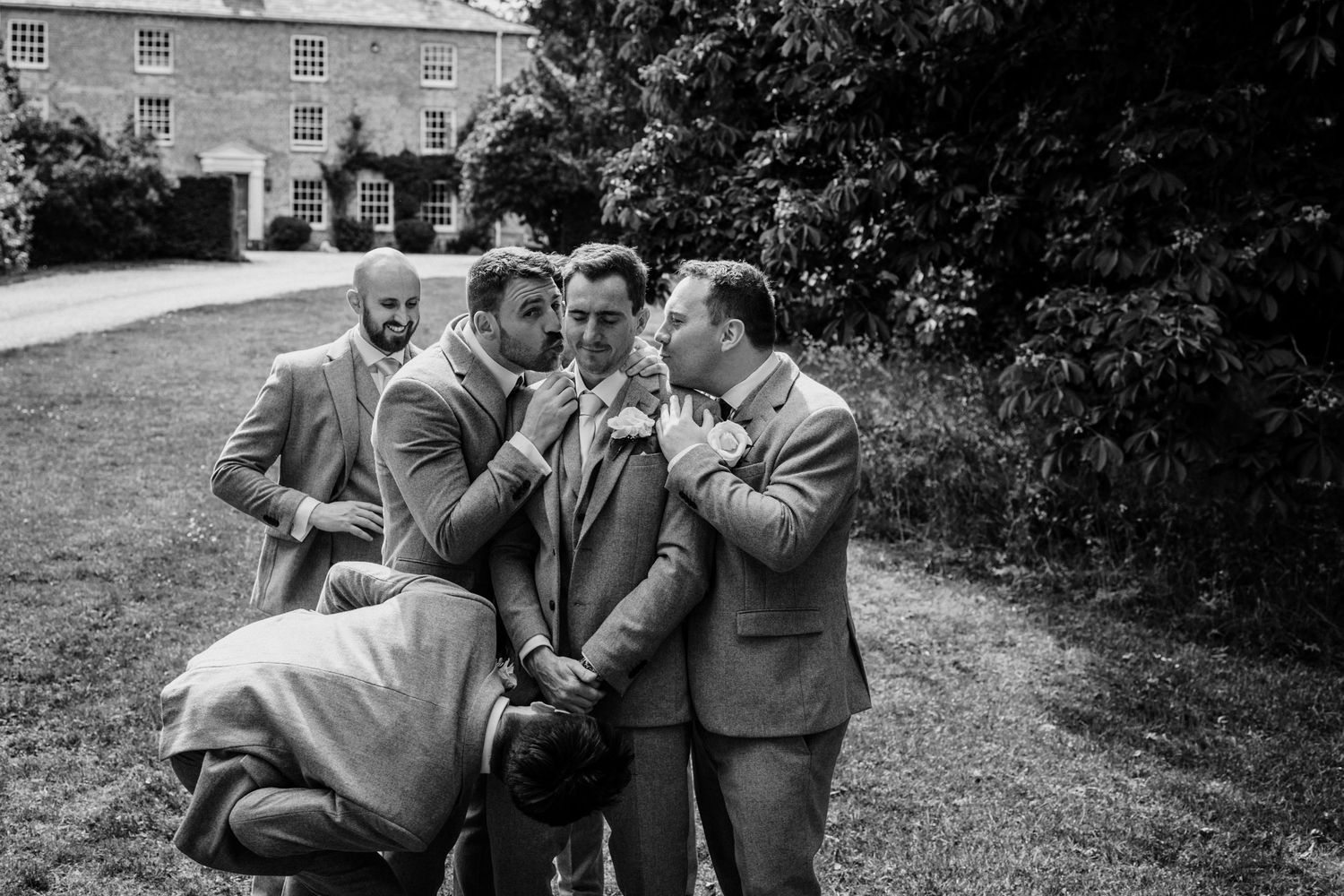 Black and white photos showing groomsmen sharing laughs outside a stone building.