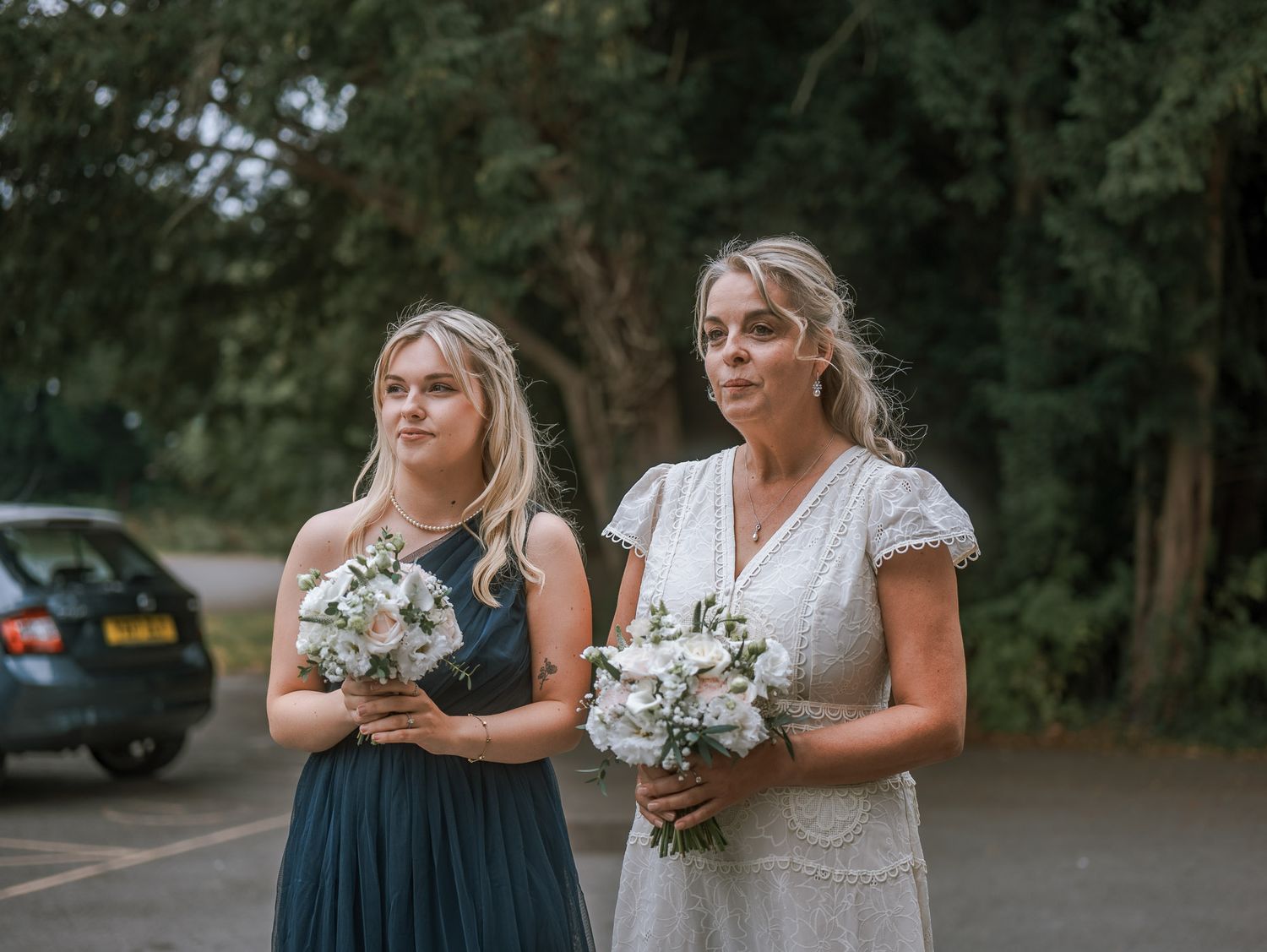 Bridesmaids in dark dresses holding bouquets outside a venue.