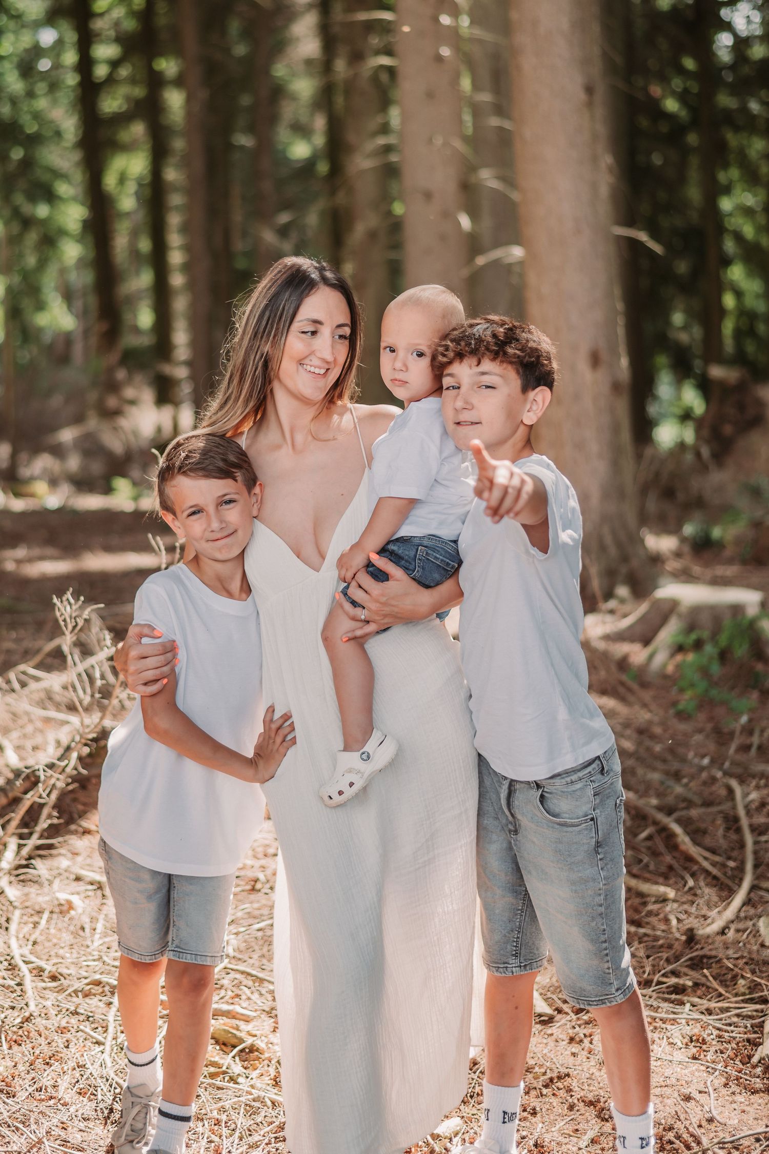 Family portrait session in a sunlit forest with children in casual summer attire.