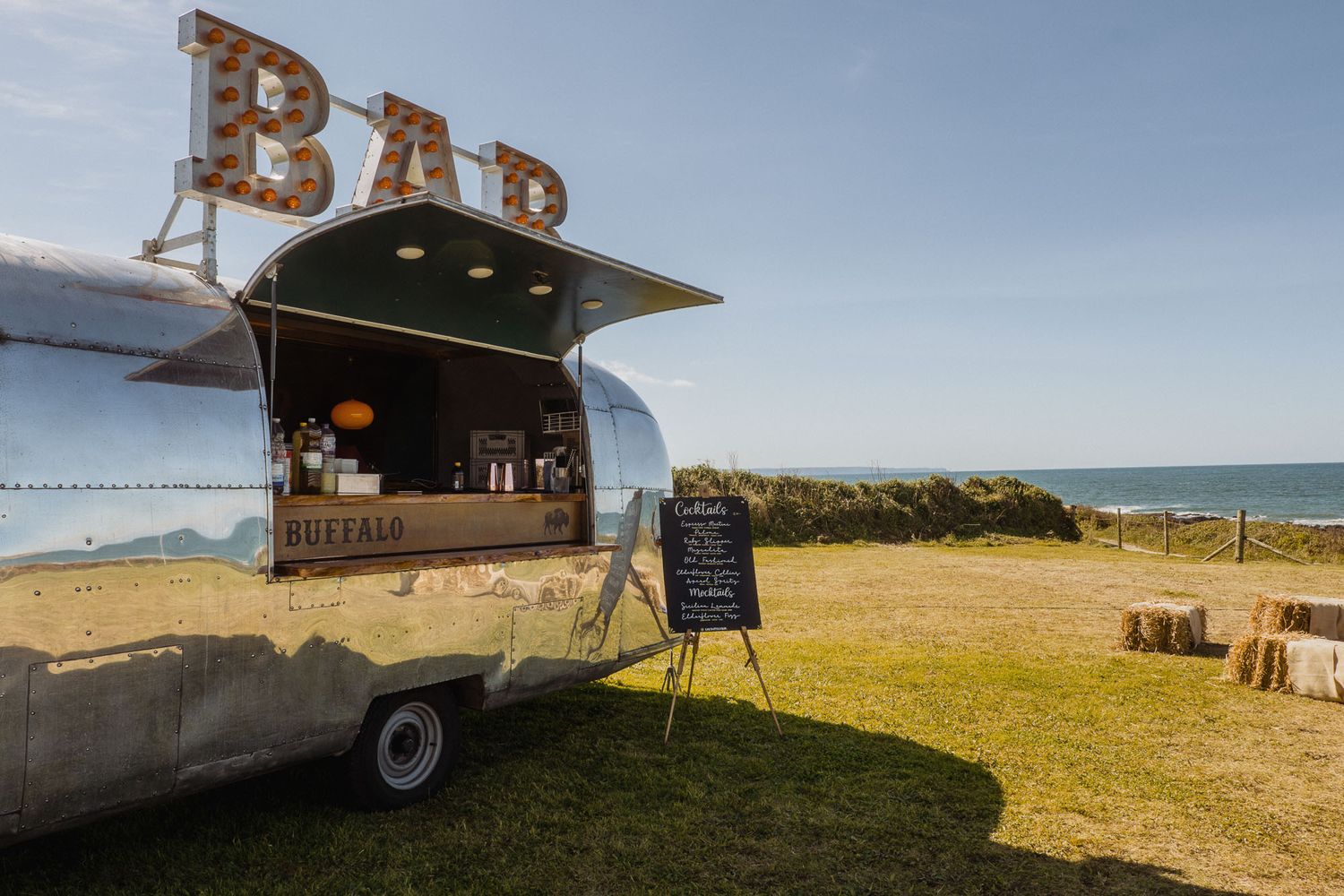 Panoramic view of outdoor bar setup in sunny field with hay bales.