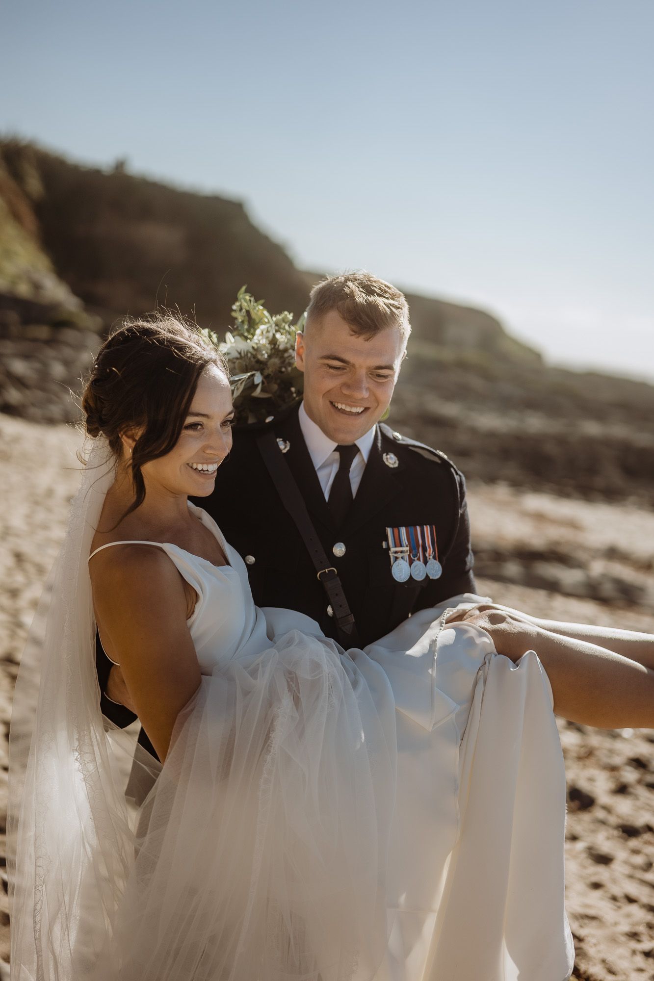 Romantic beachside wedding photography with flowing white dress and military uniform.