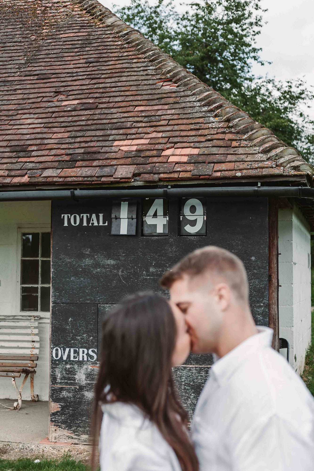 Romantic couple in white outfits sharing intimate moment against rustic building exterior.