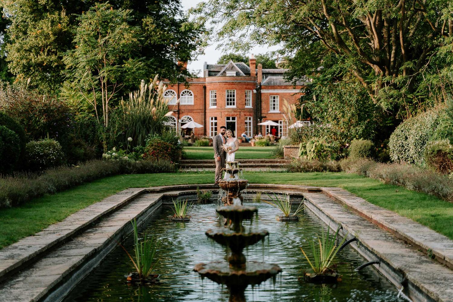 Elegant manor house with formal garden and reflecting pool featuring ornate fountain.