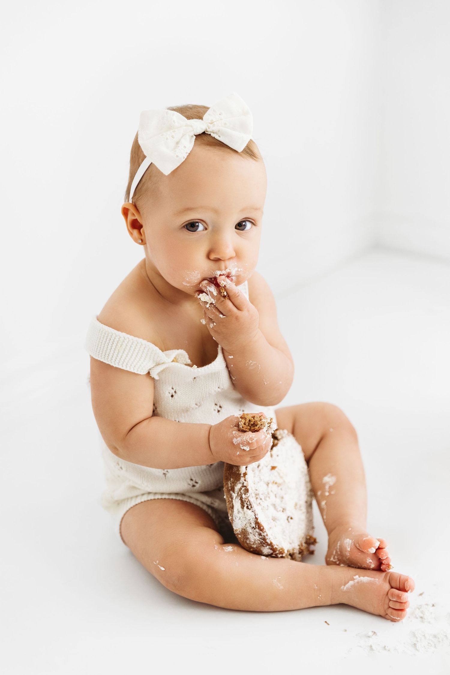 Baby Girl with a cake in her lap, eating a big handful as she looks at the camera