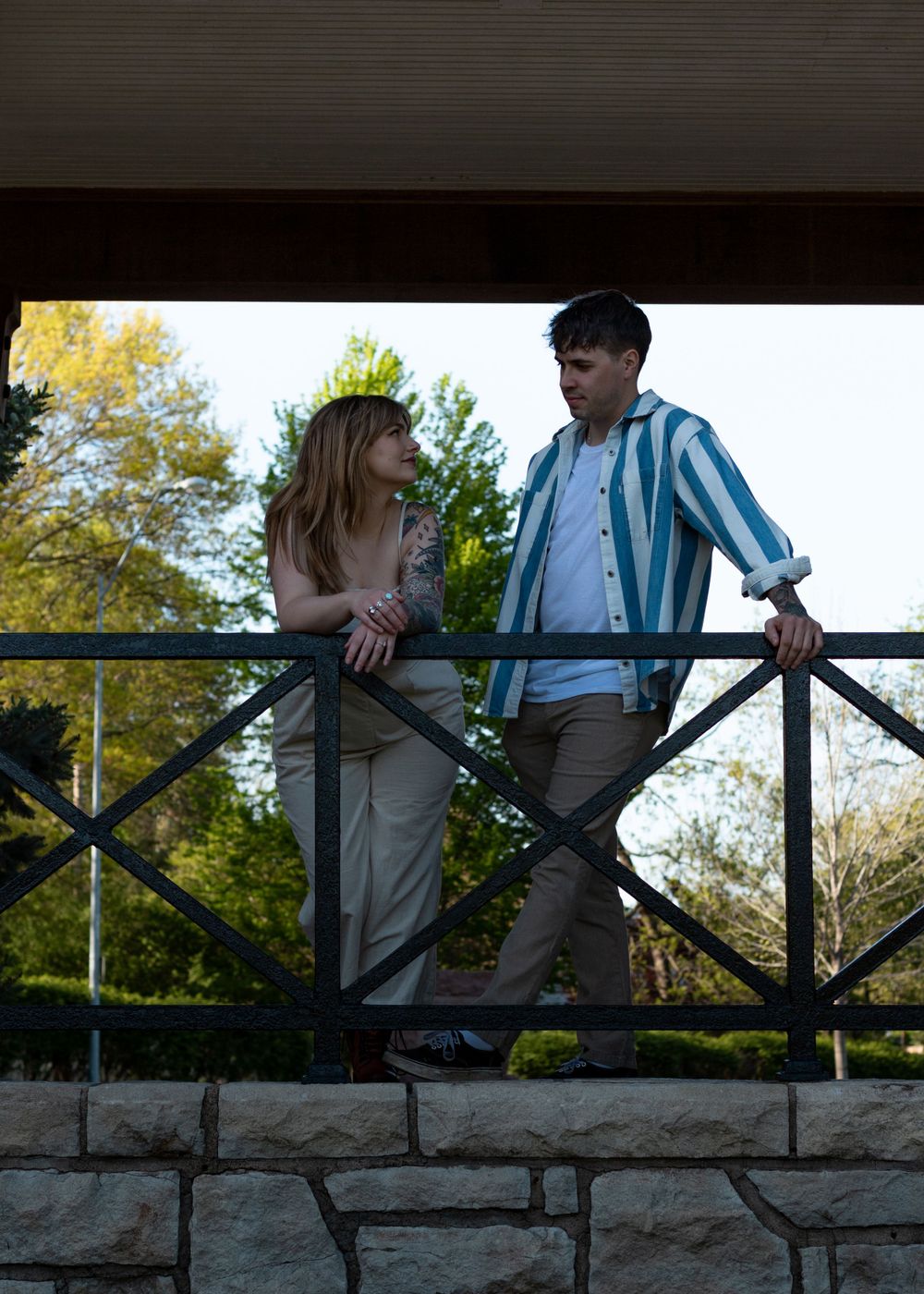 A couple leans against a stone wall railing in a romantic outdoor setting during golden hour.