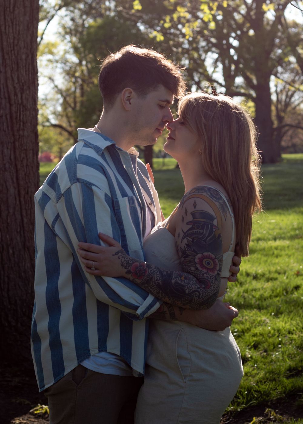 Two people share an intimate moment in a grassy field with trees in the background.