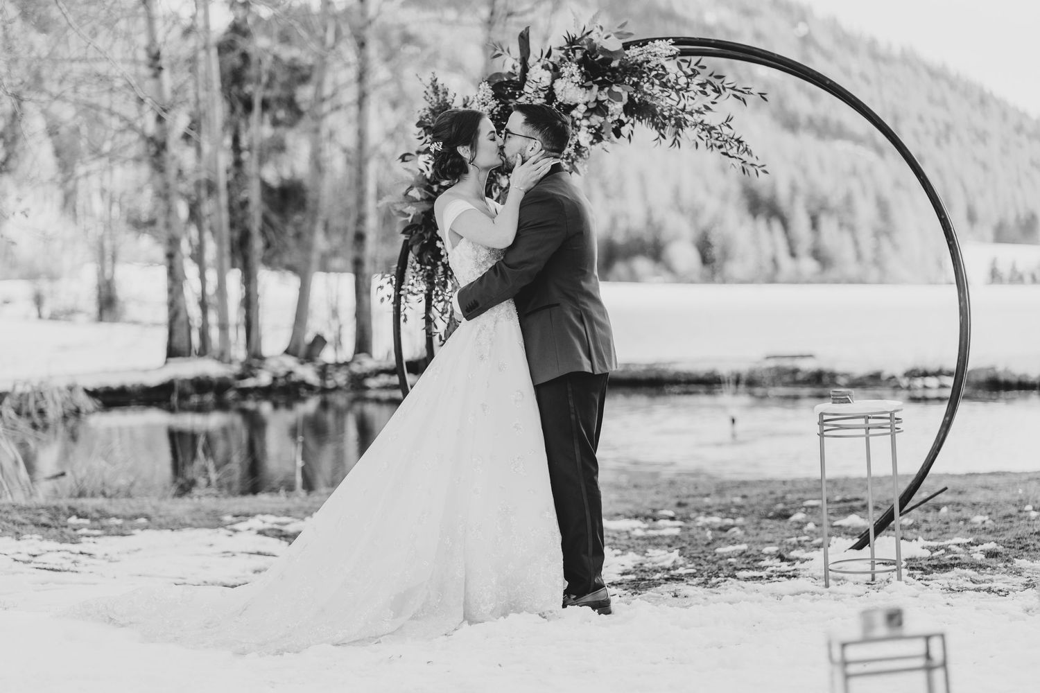 A black and white wedding portrait under a decorated arch in a winter setting.