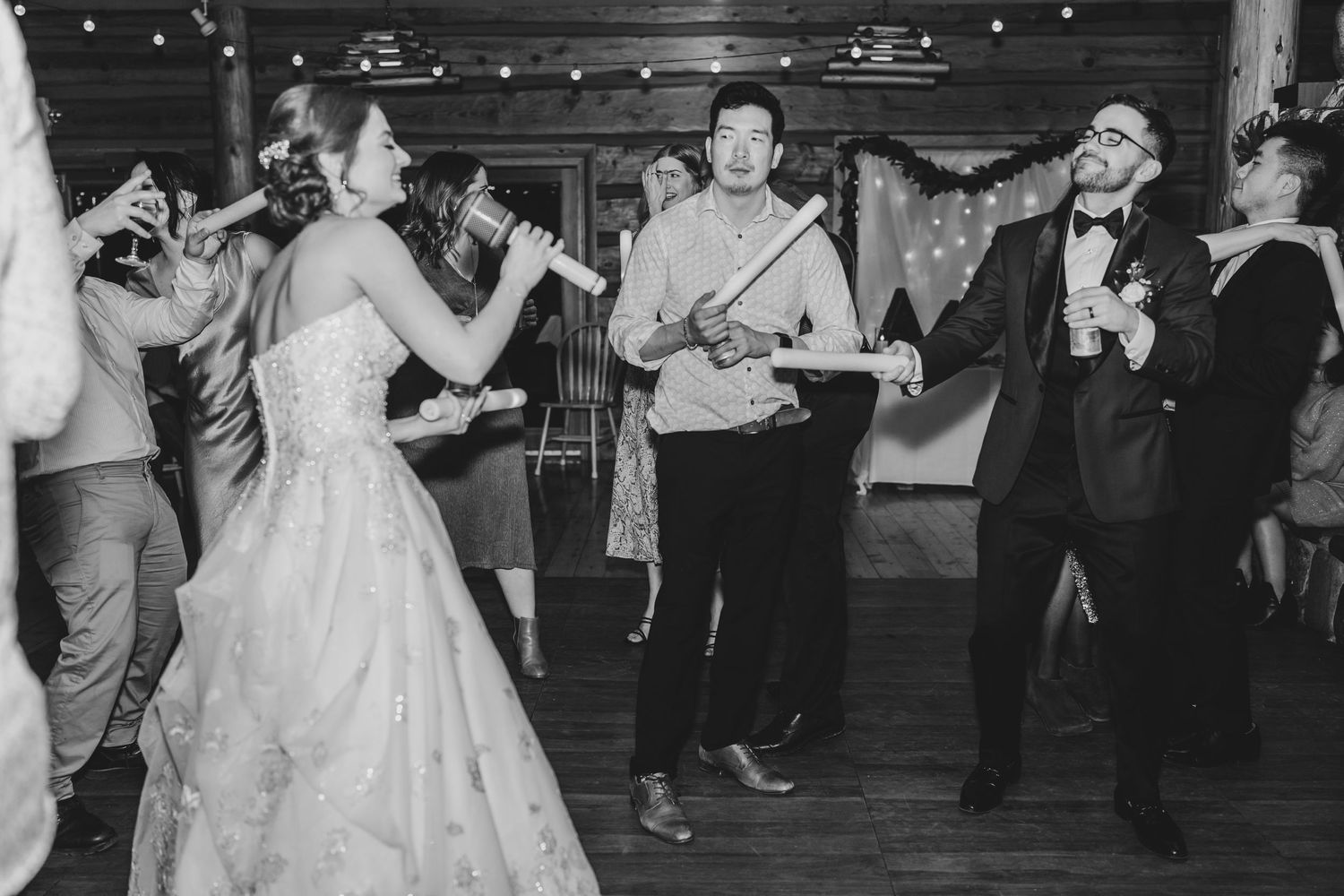 A black and white photo of wedding reception dancing in a rustic venue with string lights.