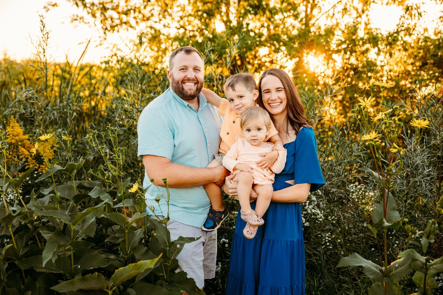 Family poses together in sunlit field during golden hour summer photoshoot.