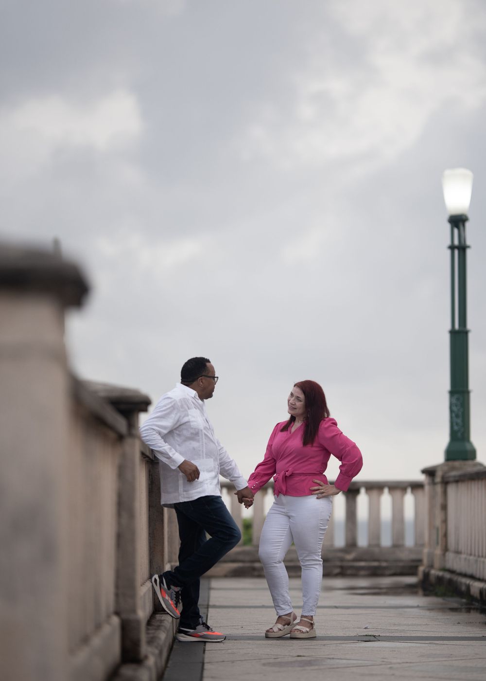 A couple shares a playful moment on a bridge with ornate lamp posts.