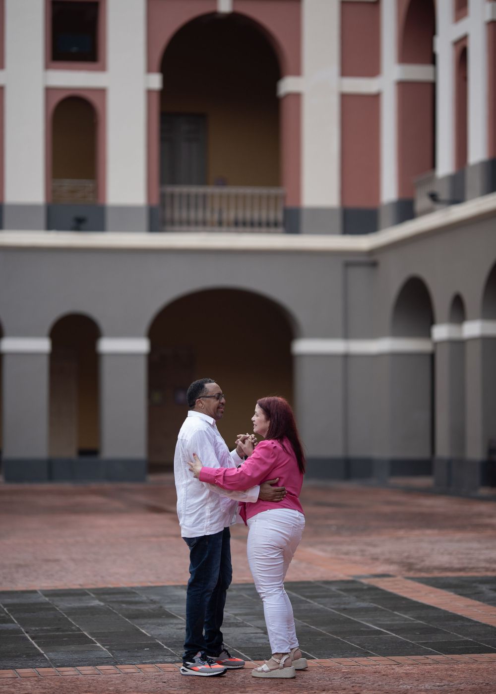 A couple dances together in a colonial courtyard with pink arched architecture.