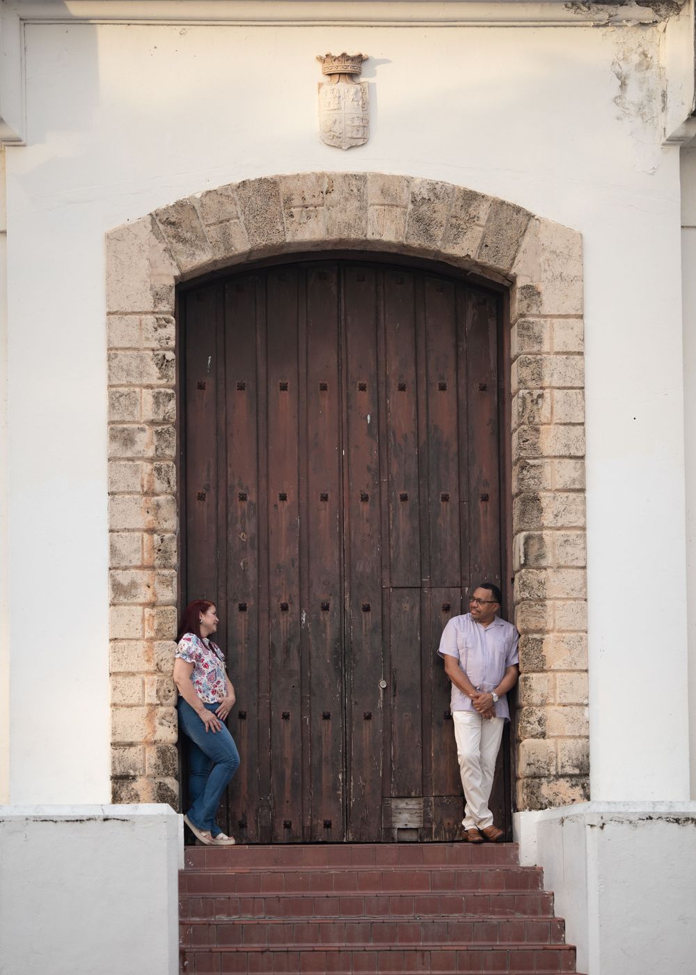 A couple poses in front of a large wooden colonial door with stone archway.