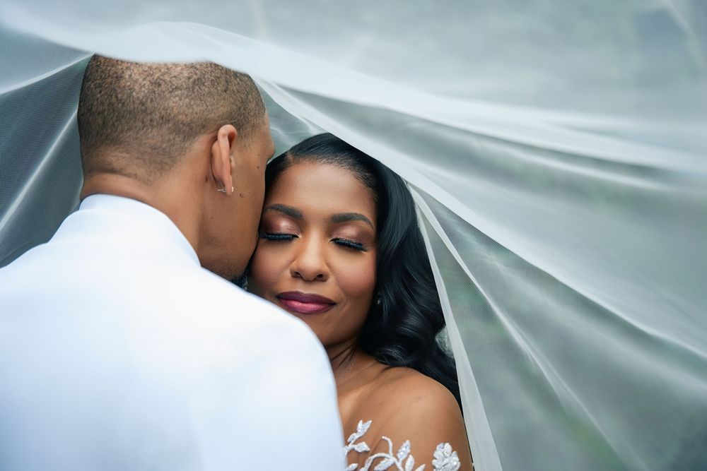 A romantic wedding moment captured under a flowing veil with soft lighting and ethereal atmosphere.