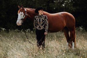 Rød-hvid hest med western-grime og dame ved siden af med show-westerntøj og cowboyhat