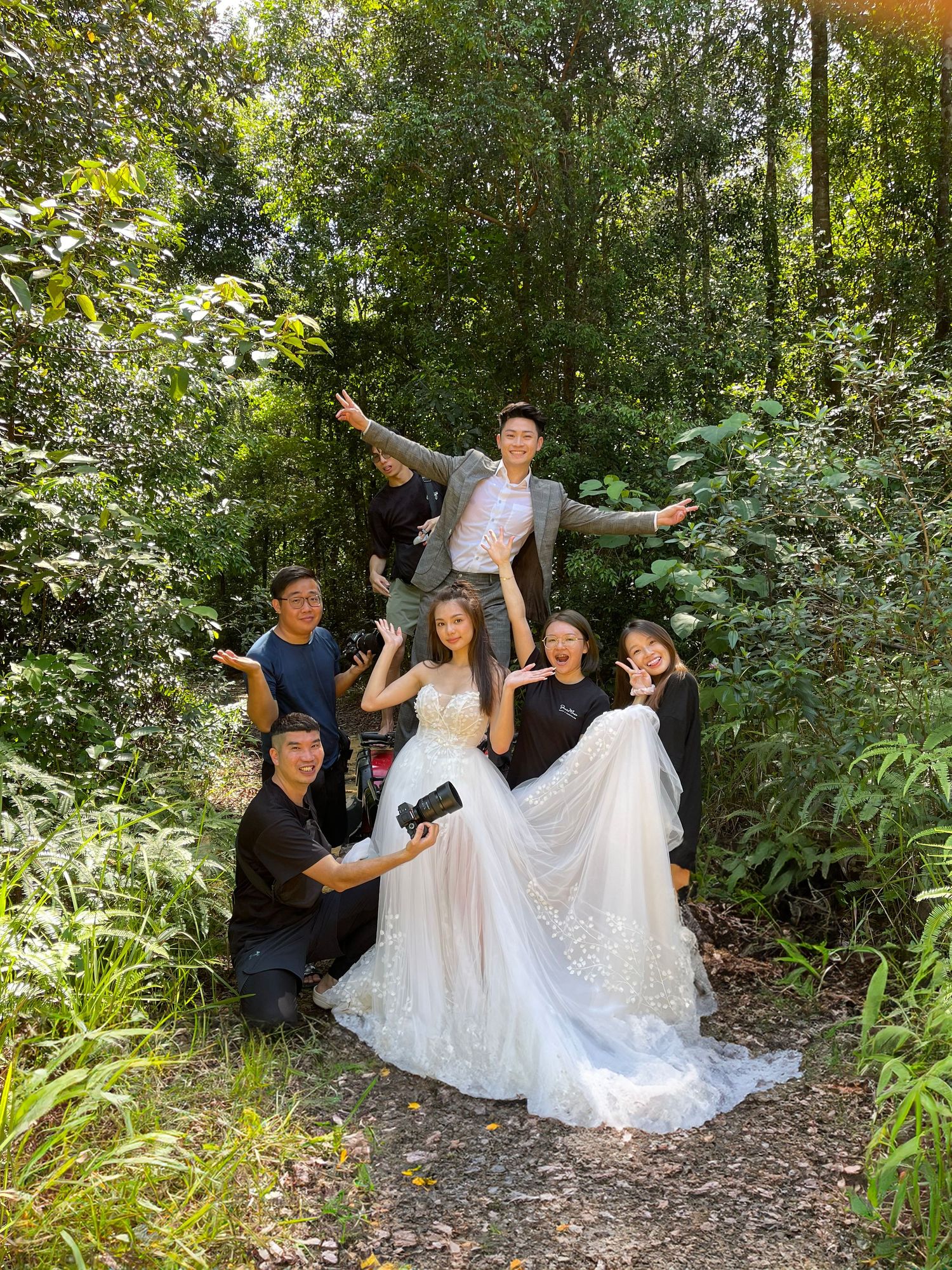 Wedding party having fun during outdoor photoshoot with white dresses in lush garden setting.