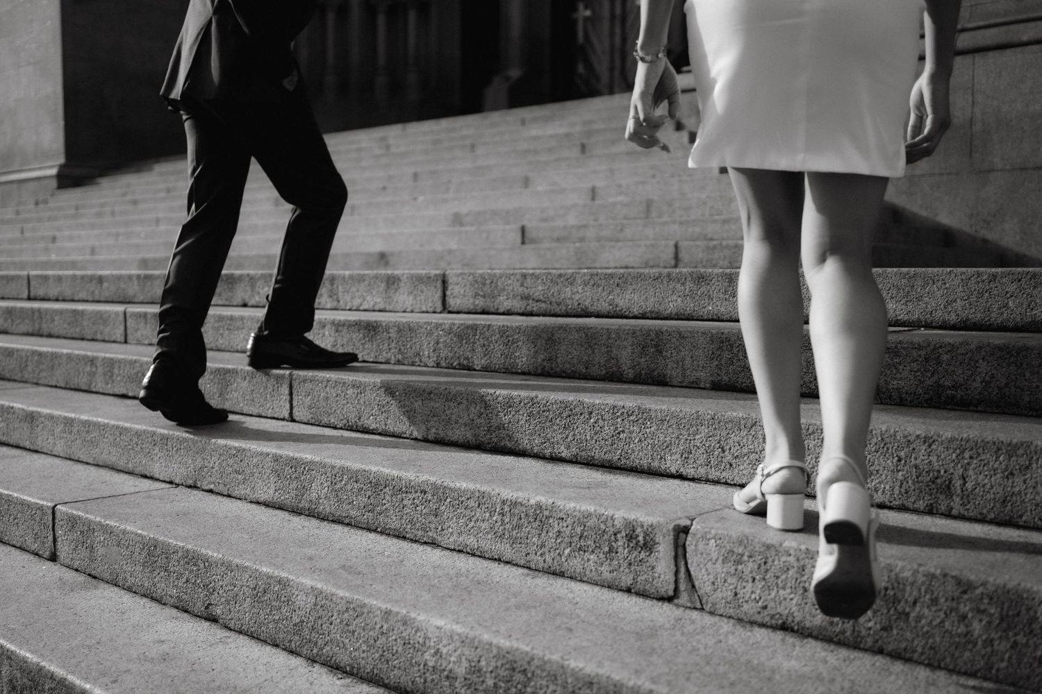 Black and white view of two sets of legs walking up stone steps.