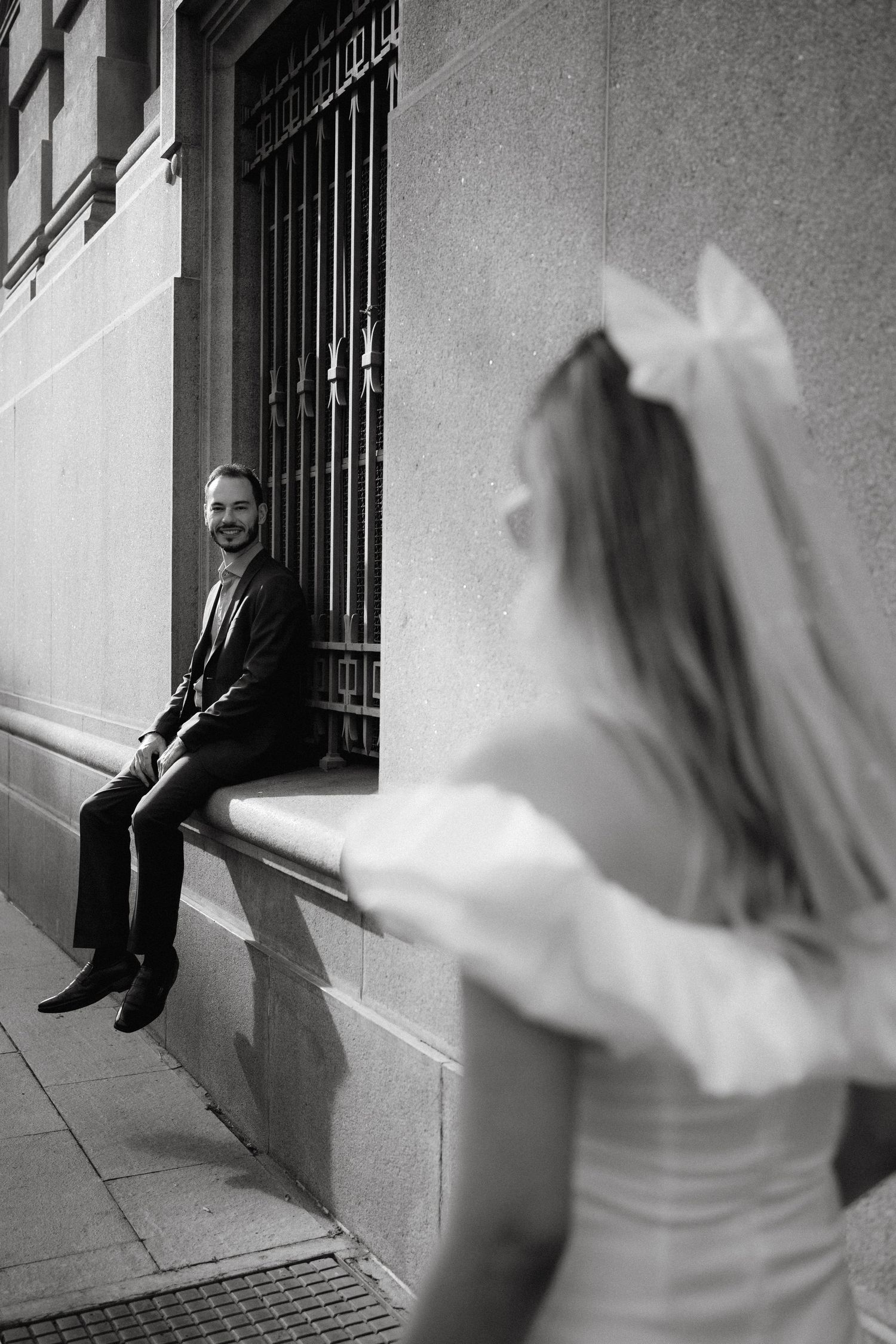 Black and white photo of a couple posing by an old building with iron window bars.