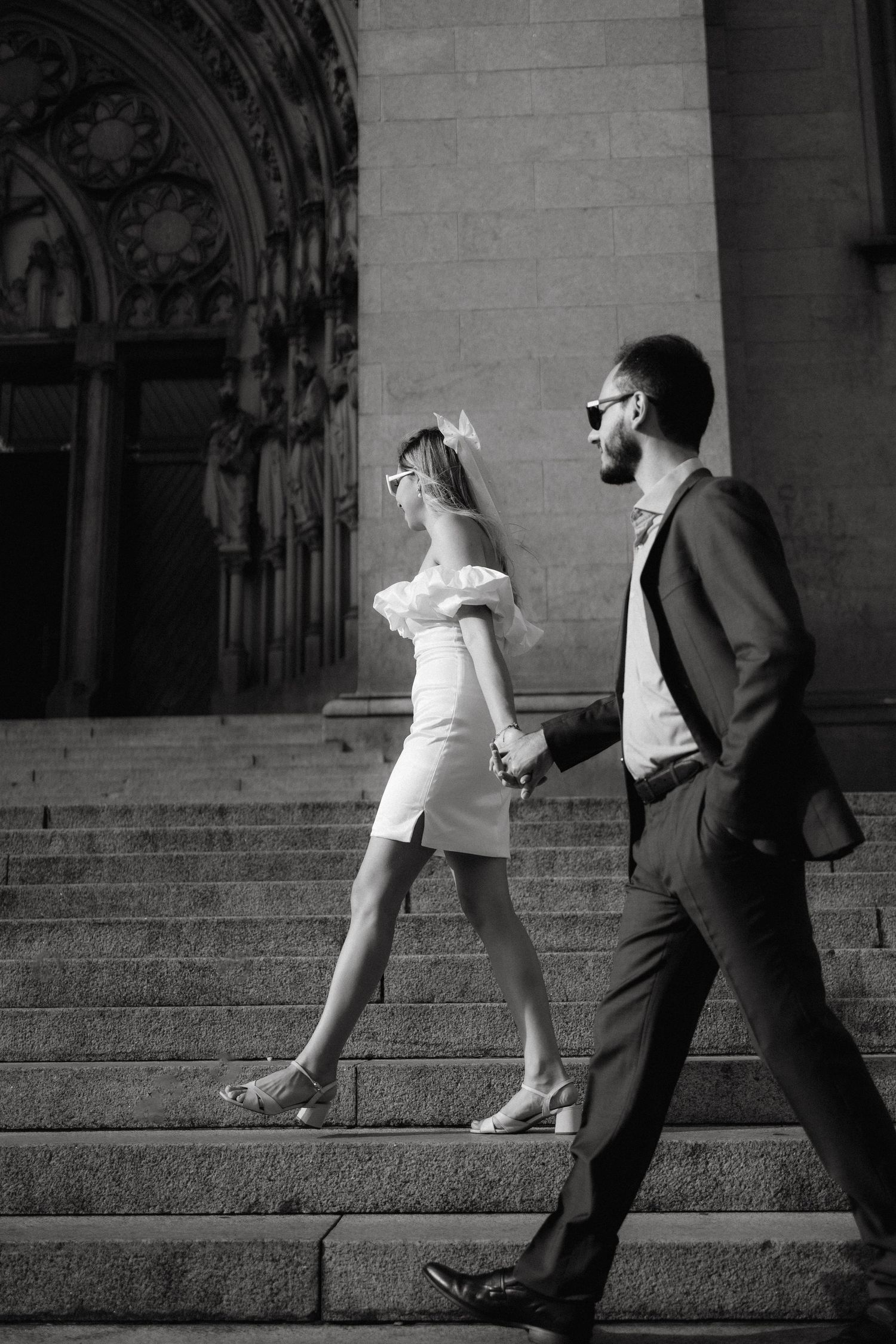Elegant couple walking up ornate cathedral steps in black and white photography.