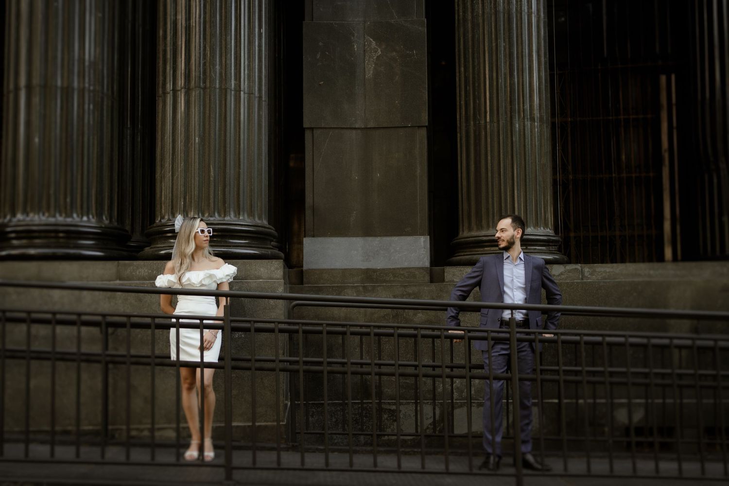 Couple posing against massive stone columns of a classical building.