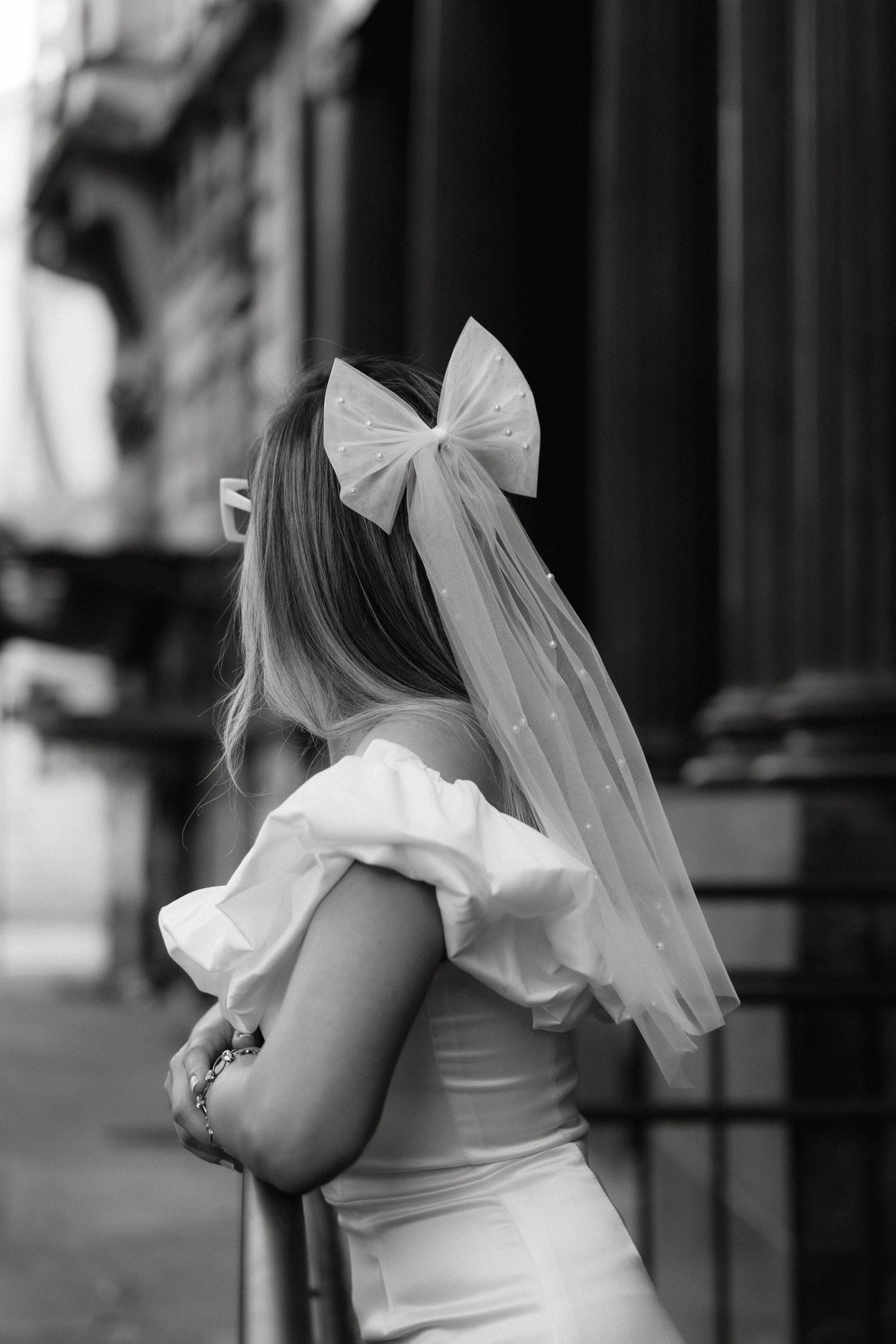 Black and white detail of bridal veil with bow against urban architecture.