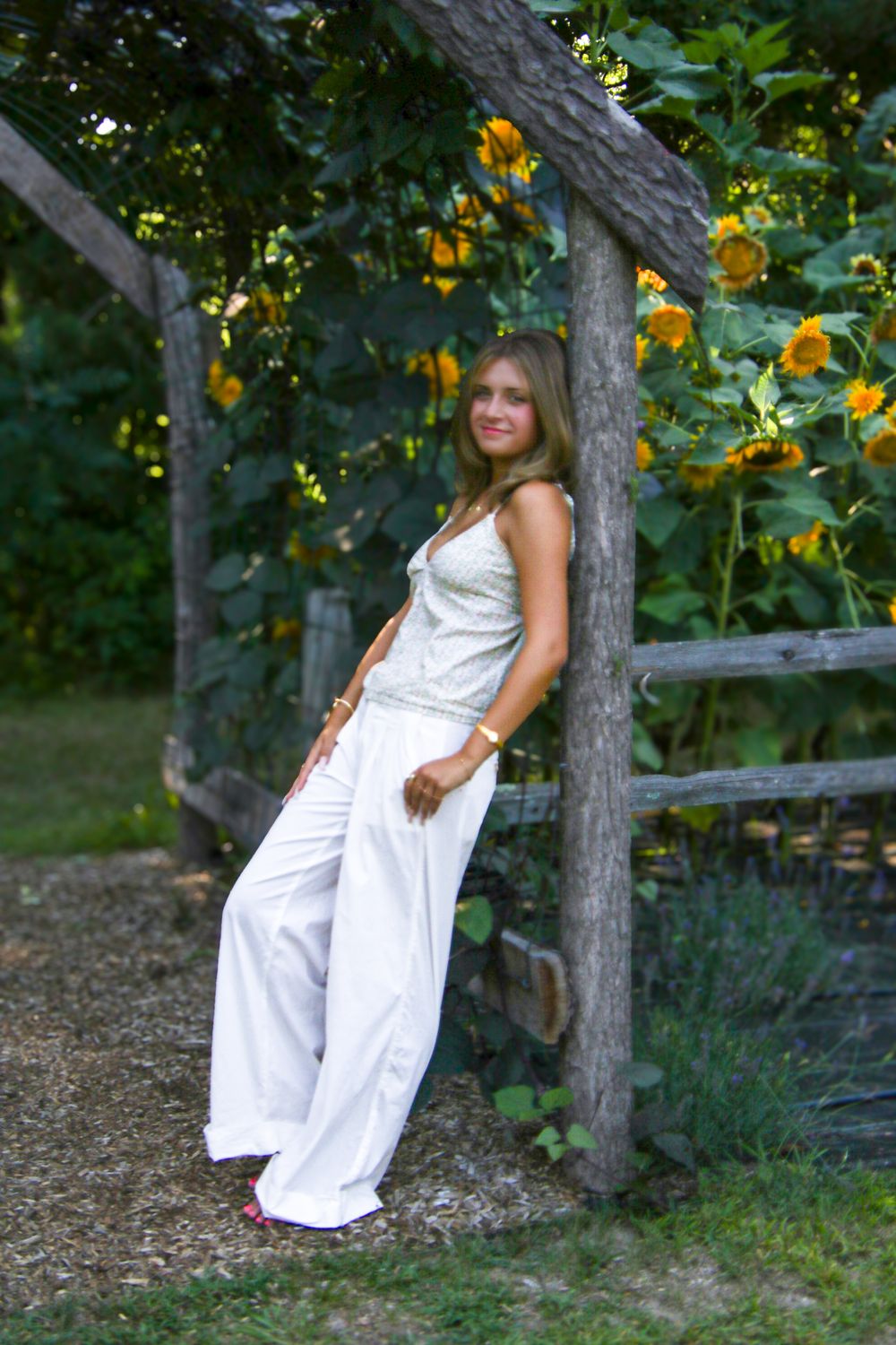 White summer outfit styled against rustic wooden fence and sunflower garden backdrop.