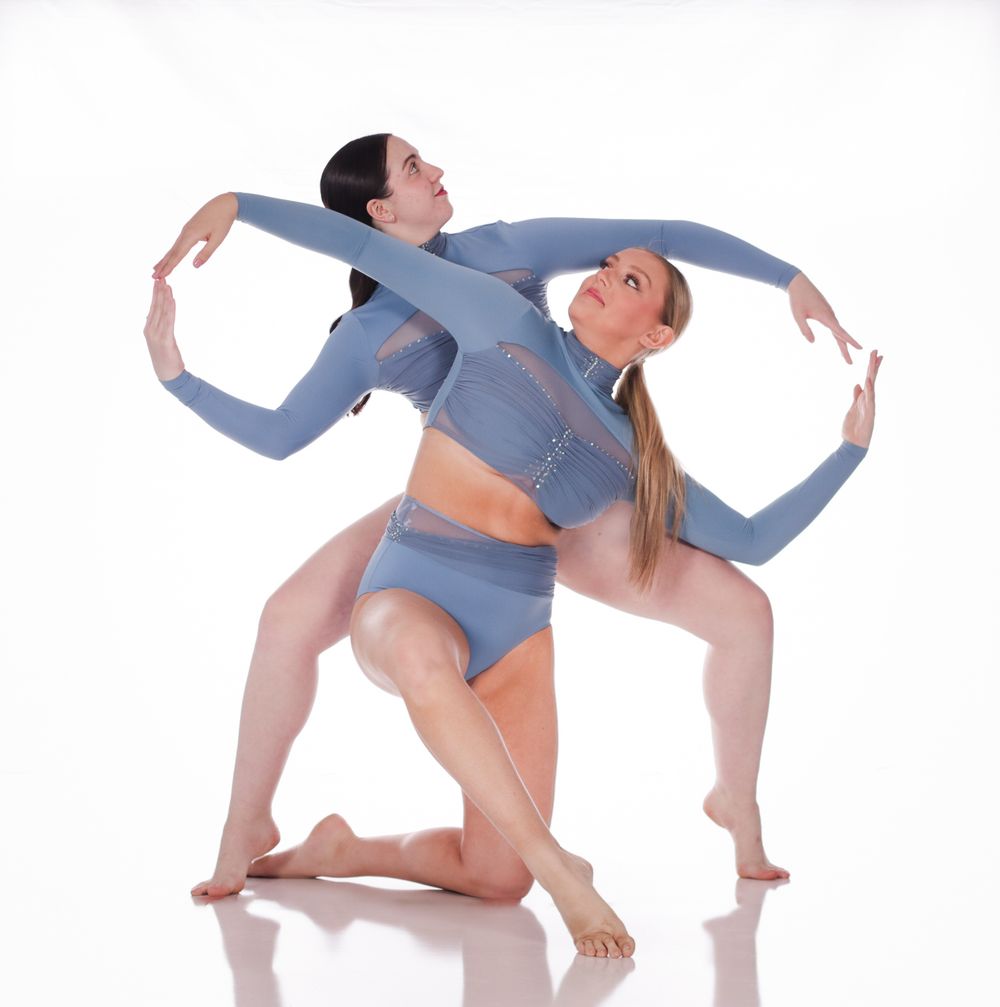 Two dancers in blue leotards perform a contemporary dance move together.