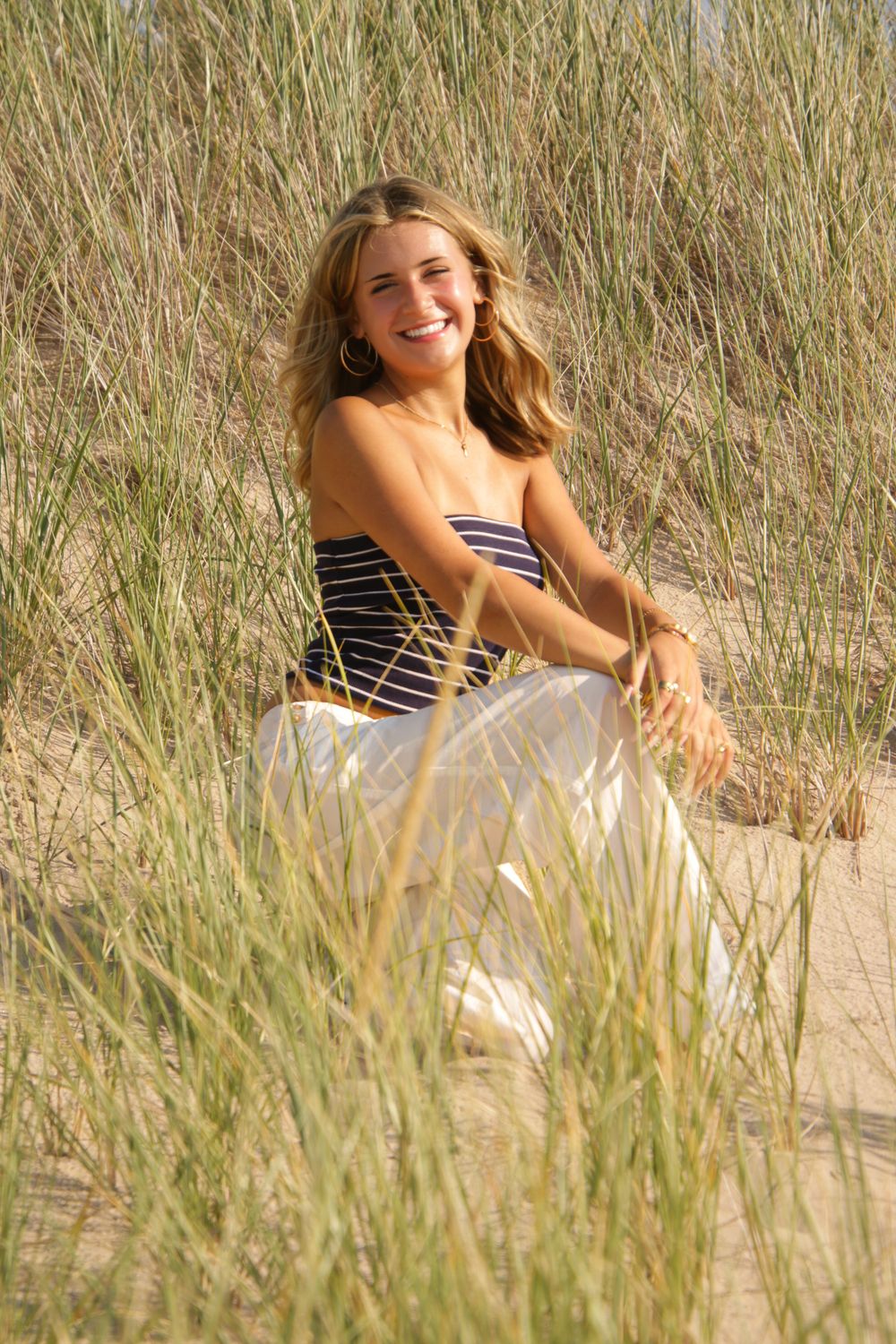 Person relaxing among tall beach grass on sandy dunes near ocean.