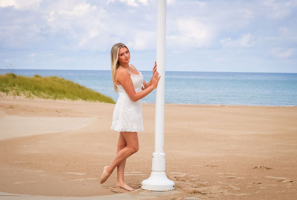 Sandy beach scene with white lighthouse post and ocean waves in background.