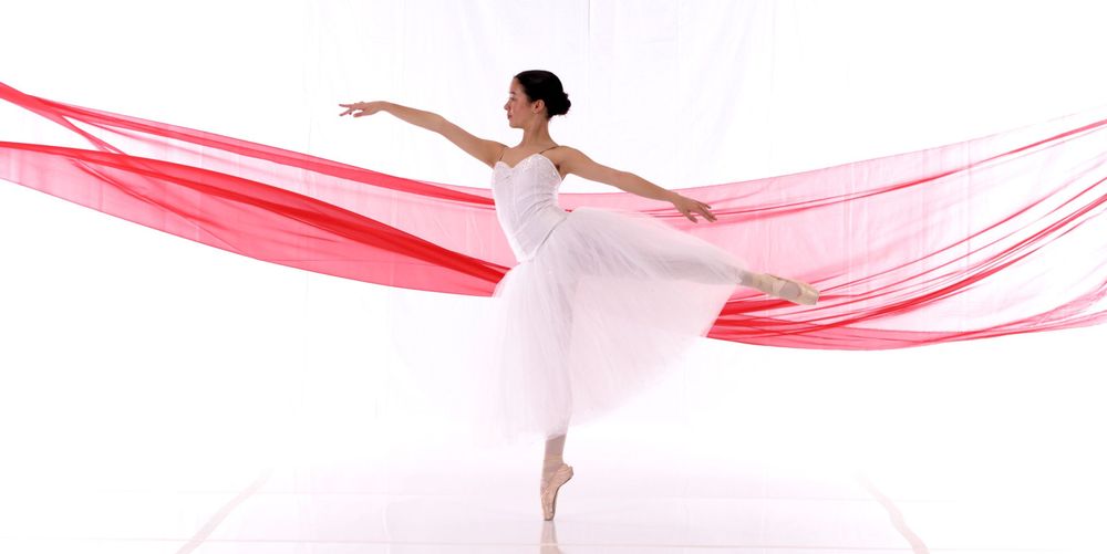 A ballet dancer en pointe with flowing red fabric creates an elegant silhouette.