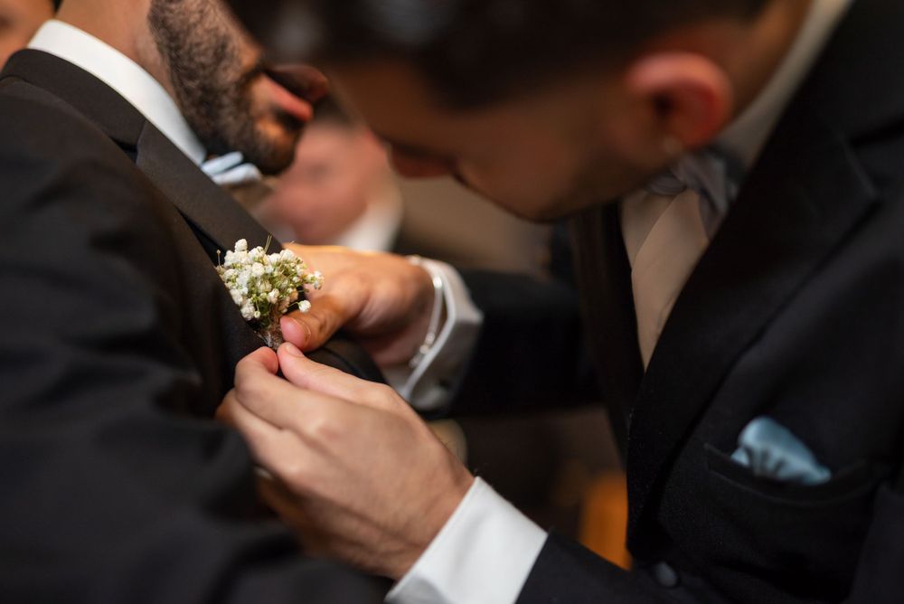 Close-up of groomsman helping pin boutonniere on suit lapel.