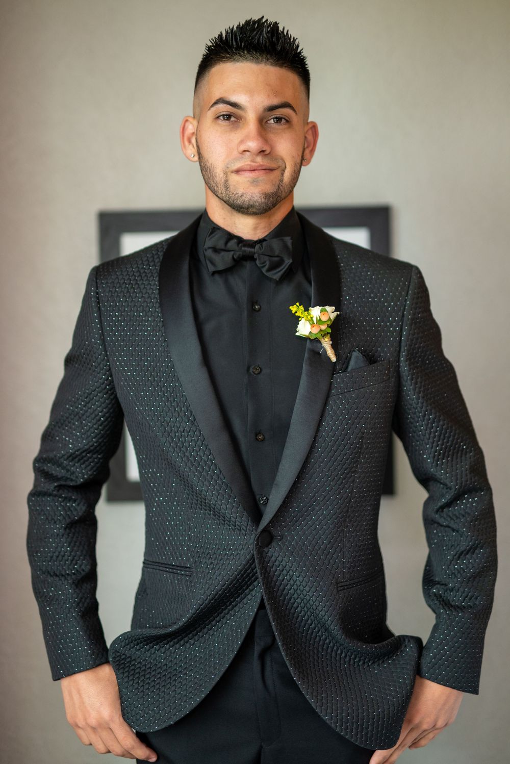 Groom in a black textured tuxedo with bow tie and floral boutonniere.