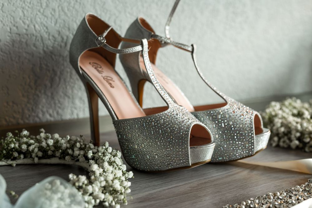 Sparkling silver peep-toe bridal heels with ankle straps on wooden surface.