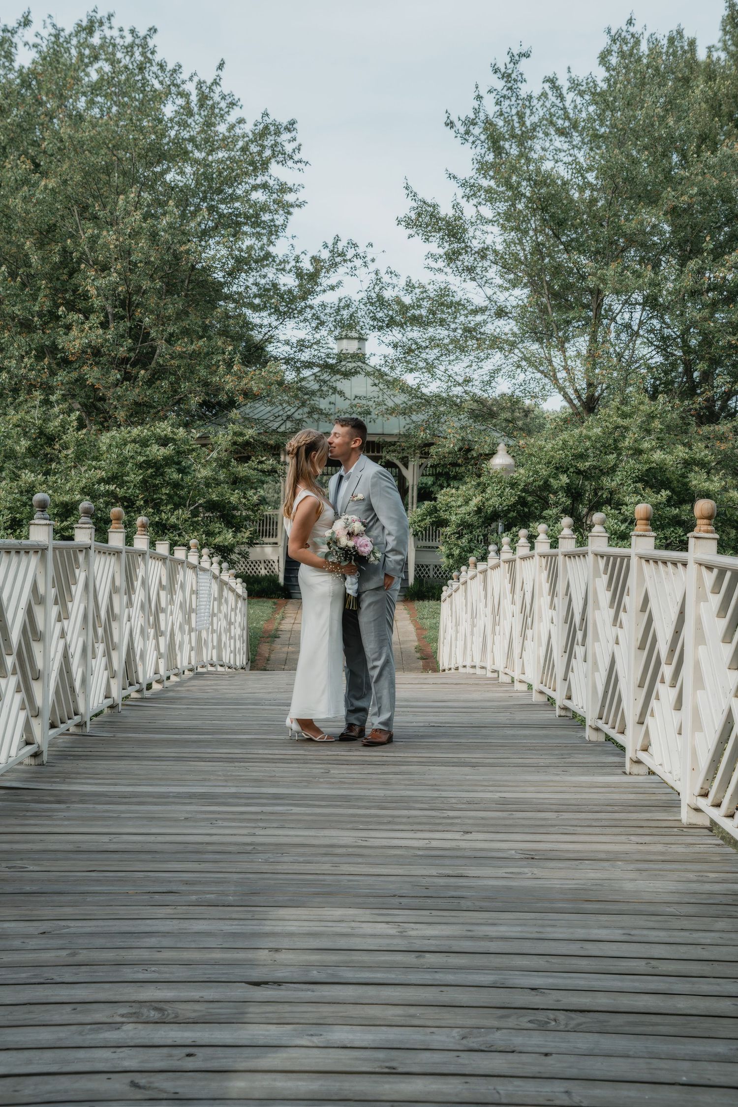 A romantic moment on a white wooden bridge surrounded by lush greenery.